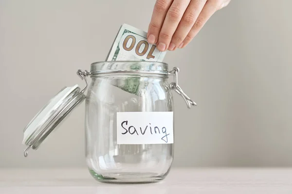 Femme main nous tenant billet d'un dollar et mettre dans un bocal en verre avec inscription sauver. Économiser de l'argent et concept de budget domestique — Photo