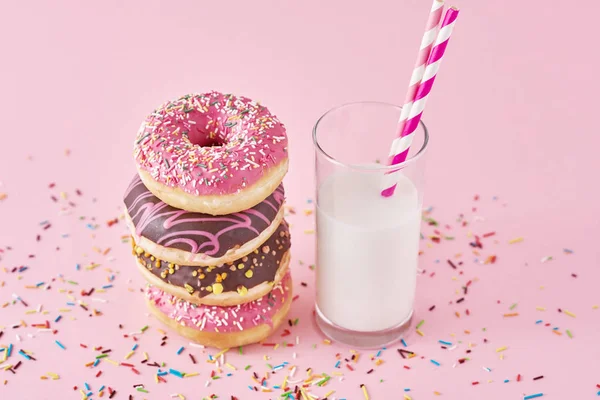 Stack of colorful donuts decorated and glass of milk on a pink background — Stock Photo, Image