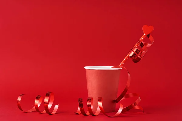 Taza de café de papel con corazón de madera en paja y cintas festivas en el fondo rojo. Concepto de San Valentín — Foto de Stock