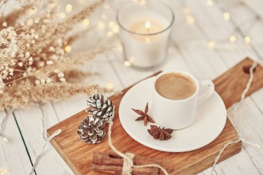 Üzerinde çelenk ışıkları, yanan mum ve dekorasyon olan bir fincan kahve. Konforlu ev kavramı