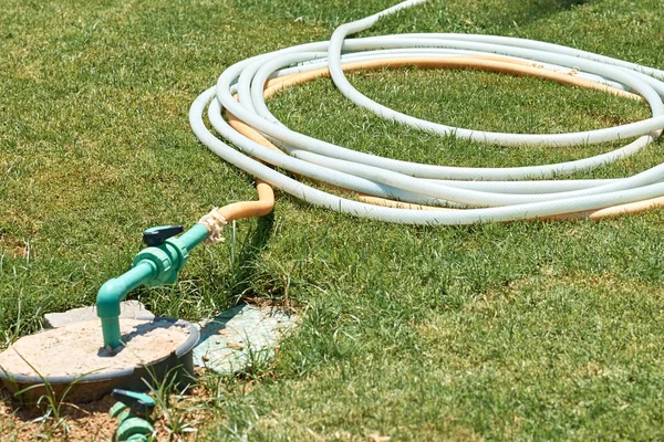 Wąż nawadniający skręcony na zielonej trawie w letni dzień — Zdjęcie stockowe