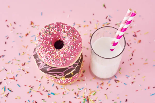 Stack of colorful donuts decorated and glass of milk on a pink background — Stock Photo, Image