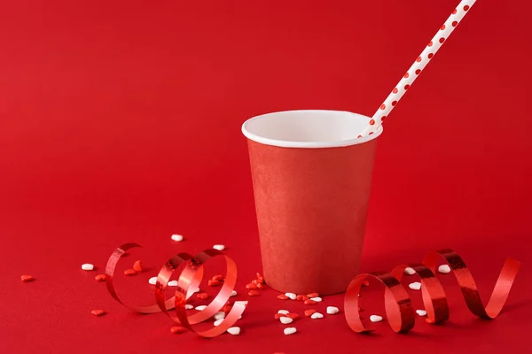 Taza de café de papel con decoraciones festivas y confeti en el fondo rojo — Foto de Stock