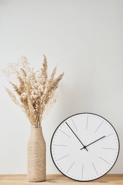 Klasik yuvarlak saat ve ahşap masa üzerinde kurutulmuş bitki içeren ev yapımı vazo.