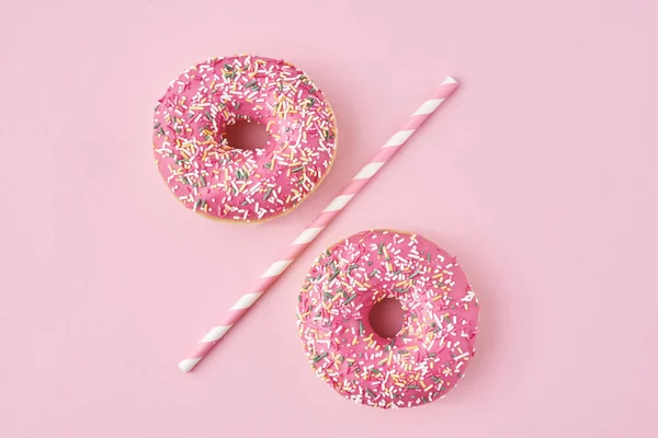 Twee donuts gescheiden met een rietje op roze achtergrond. Creatief voedselconcept — Stockfoto