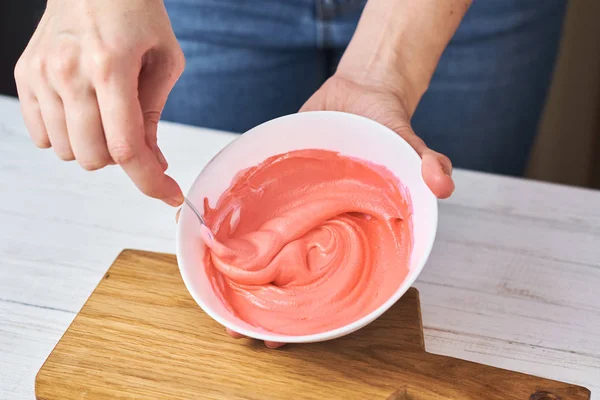 Mujer batiendo crema roja para decorar galletas en un tazón en la cocina, primer plano —  Fotos de Stock