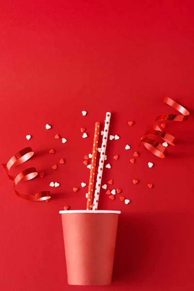 Taza de café de papel con decoraciones festivas y confeti en el fondo rojo, la vista superior plana laico. Concepto de minimalismo creativo — Foto de Stock