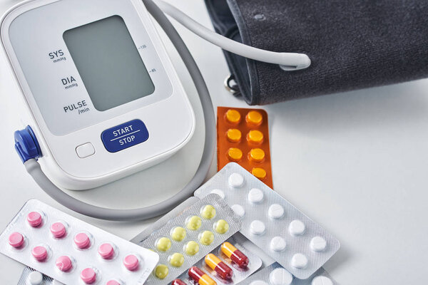 Digital blood pressure monitor and medical pills on the white table. Healthcare and medicine concept