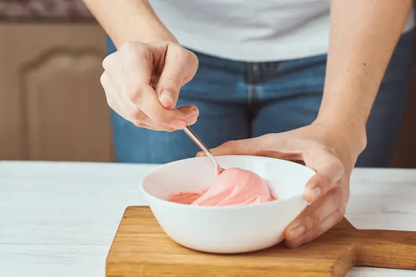 Mujer batiendo crema roja para decorar galletas en un tazón en la cocina, primer plano —  Fotos de Stock