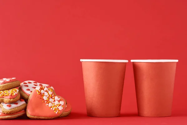 Galletas decoradas en forma de corazón y dos tazas de café de papel sobre el fondo rojo. Concepto de comida de San Valentín — Foto de Stock