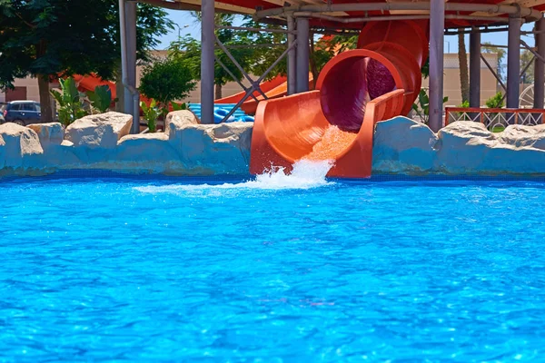 Corrediça de parque aquático vermelho e uma piscina. Aqua parque fundo — Fotografia de Stock