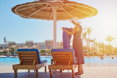 Kadın otelin havuzunun yanındaki güneşli yatağa havlu seriyor.