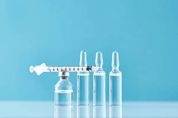 Spritzen und Medizinflaschen mit Medikamenten auf blauem Hintergrund — Stockfoto