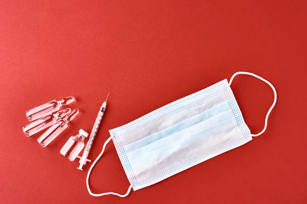 Medical syringe, ampoule with medicine and protect mask on the red background, top view. Vaccination and epidemic virus protection concept. — 스톡 사진