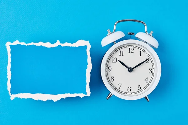 Beyaz alarm saati ve boş yırtık kağıt levha mavi bir arka grubunda — Stok fotoğraf