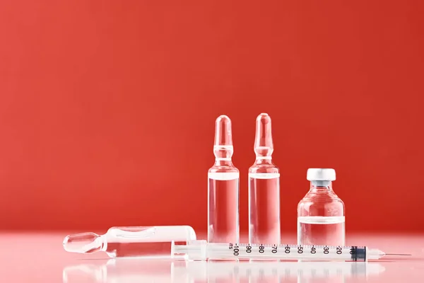 Injekční stříkačky a lahvičky s léky na červeném pozadí — Stock fotografie