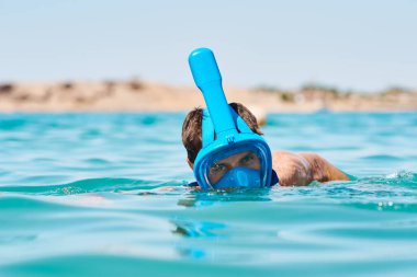 Mavi denizde yüzükoyun yüzen şnorkeli olan bir adam. Yaz tatili