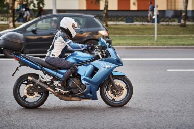 Şehir caddesinde motosiklet süren bir sürücü. Kasklı motorcu mavi bisiklet kullanıyor. Yoldaki güvenlik.