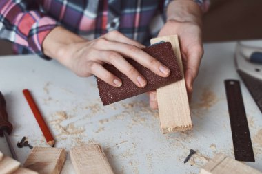 Marangoz elleri zımpara kağıdıyla tahta cilalıyor. Diy ahşap işçiliği ve mobilya yapımı kavramı