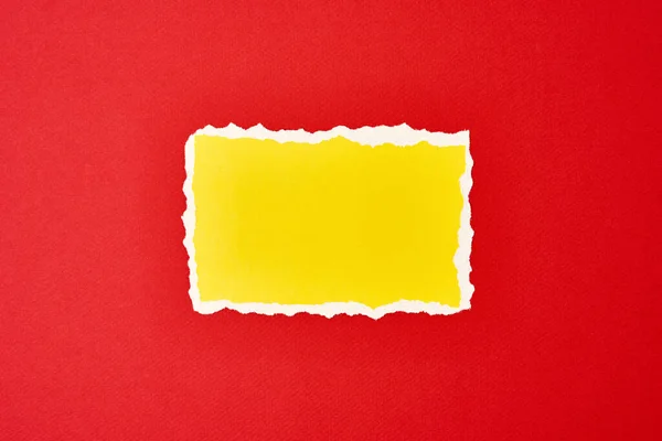 Ripped yellow paper torn edge sheet on red background. Template with piece of color paper