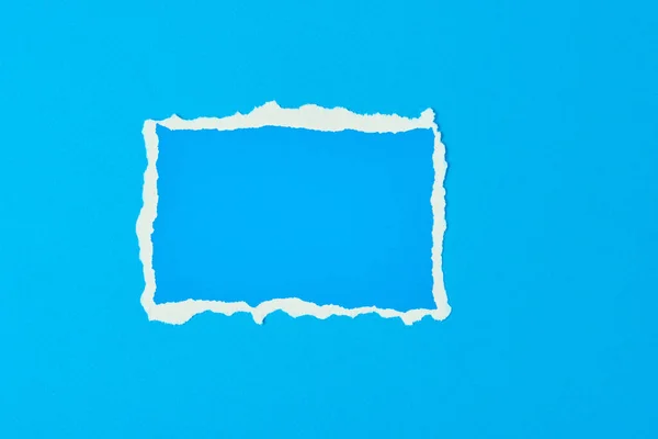 Ripped paper torn edge sheet on blue background. Template with piece of color paper