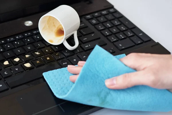 Hand cleans spilled coffee on laptop keyboard with rag