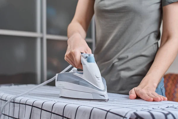 Woman ironing clothes on ironing board with modern iron