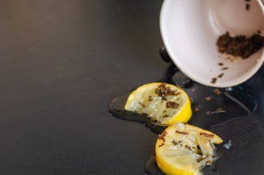 Masadaki küçük çay havuzunda iki dilim limon. Koyu bir masada ters çevrilmiş bir fincan çay. Göz hizasında atış. Seçici odak.