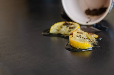 Masadaki küçük çay havuzunda iki dilim limon. Koyu bir masada ters çevrilmiş bir fincan çay. Göz hizasında atış. Seçici odak.