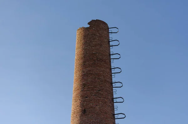 Zničený tovární komín. Červená cihlová trubka proti modré obloze. — Stock fotografie