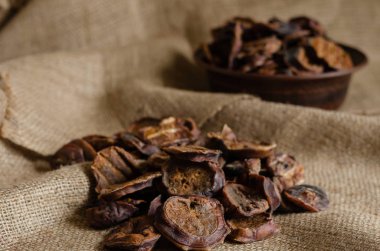 Ön planda bir grup kurutulmuş boğa testisi. Arka planda dilimlenmiş doğal malzemelerle dolu bir kil kase var. Yakın plan. Seçici odak.