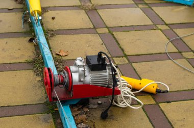 Used electric winch stands on the ground with the cover removed. Lifting equipment with a remote control. Disconnected from the mains. Selective focus.
