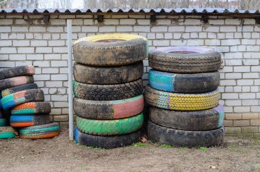 Painted old truck tires. Many colorful tires against a white brick wall. Outside Without anyone