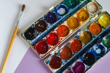 Resim için kullanılmış suluboya boya ve fırça seti. Çok renkli bir masada yaratıcılık için aksesuarlar. Yukarıdan bak. Seçici odaklanma. Hiç kimse olmadan.