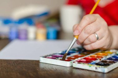 Selective focus of a female hand soaking brush in watercolor paint