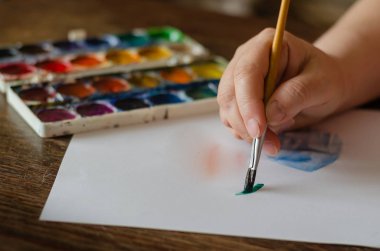Female hand draws with watercolors on a white sheet of paper. 