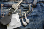 Klíč s řetízkem na klíče, sluchátky a kondomem na džínové tkanině. 