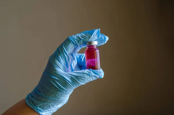 Primer plano de una botella de vidrio rosa en una mano con guantes . —  Fotos de Stock