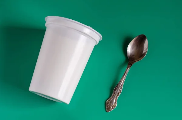 White plastic glass with yogurt and a spoon on a green backgroun — Zdjęcie stockowe