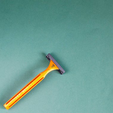 Gri-yeşil arka planda tek kullanımlık jilet. Turuncu plastik bir jiletin üst görüntüsü. Yakın plan. Seçici odaklanma. Kare bileşimi