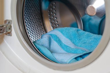 Çamaşır makinesinin içinde turkuaz havlu var. Günlük rutin ödev. Yakın plan. Seçici odak.