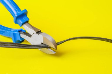 Göğüs uçları elektrik kablosunu kesmiş. Üç kablolu eski bir elektrik kablosunu kesmek. Sarı arka planda siyah kablo. Yakın plan. Seçici odak.