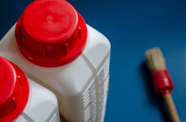 İki beyaz plastik şişe ve bir boya fırçası. Kırmızı şapkalı bir çift şişenin üst görüntüsü. Ev onarımı, tasarım veya zanaat. Yakın plan. Seçici odak.