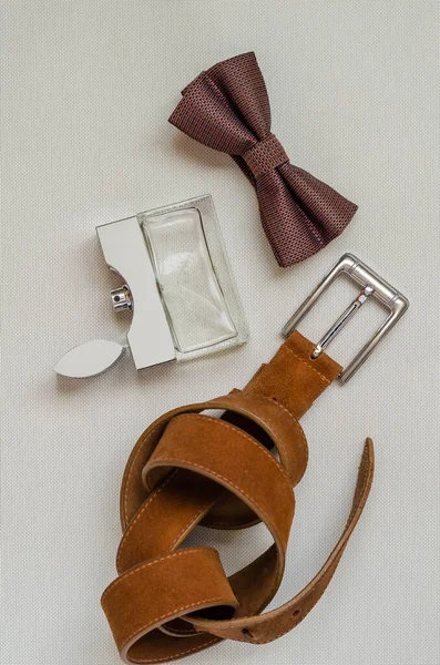 A set of elegant accessories for men. Bow tie, perfume and leather trouser belt. A gift to her husband, lover, father, boyfriend. View from above. Selective focus. Vertical photo