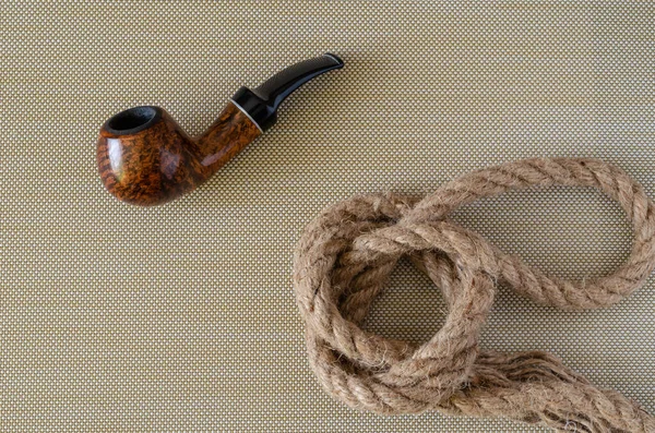 Smoking pipe and hemp rope. Briar smoking pipe and rope knot on a textured background. View from above. Sailor or fisherman concept.