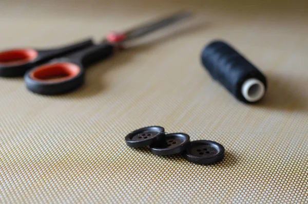 3つのボタン はさみ 糸のスプール テーブルの上にアクセサリーを縫製のセット ライトの背景にブラックアクセサリー 服の修理だ サイドビュー 前景を中心に 眼レベル撮影 — ストック写真