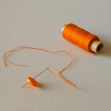 Düğme, iğne, iplik ve turuncu iplik. Masada turuncu dikiş aksesuarları var. Giysi tamiri. Yan görüş. Seçici odak.