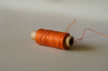 Bir makara turuncu iplik ve iğne. Masada turuncu dikiş aksesuarları var. Giysi tamiri. Yan görüş. Seçici odaklanma. Yakın plan..