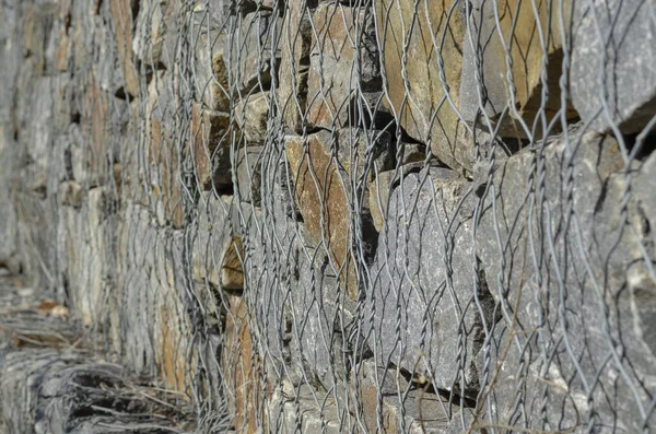 Gabion. Stone fence in a metal mesh. Crushed stone packed in wire mesh. Granite texture. Selective focus. Abstract background.