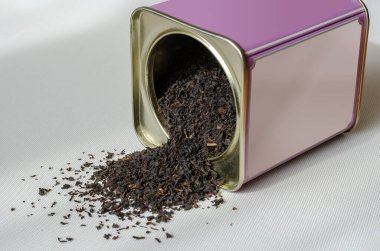 Çay için mor kutu. Mor bir teneke kutudan serpiştirilmiş kurutulmuş çay yaprakları. Açık bir metal kutu arka planda yatar. Seçici odaklanma. Göz hizası atışı.